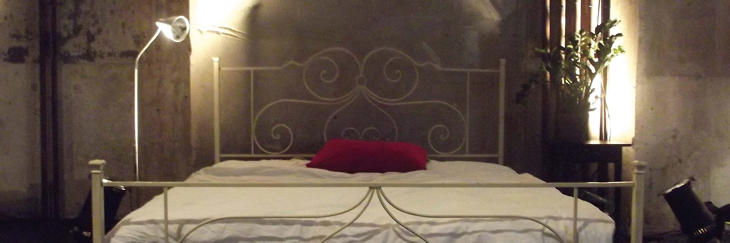 Ein weißes Doppelbett steht in einem Raum. Ein rotes Kissen liegt darauf.